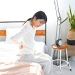 朝一、ベットの上で腰痛や背中の痛みに悩む女性