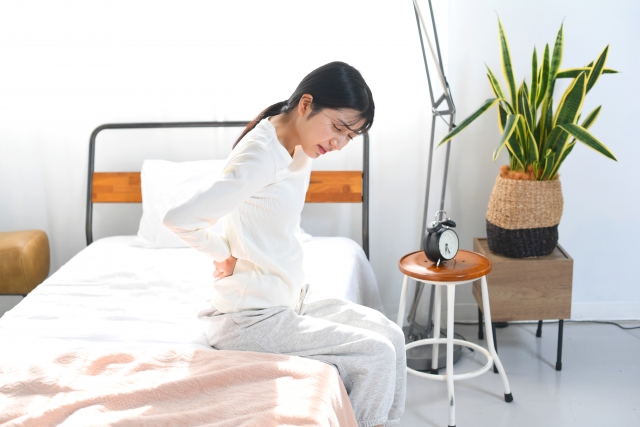 朝一、ベットの上で腰痛や背中の痛みに悩む女性